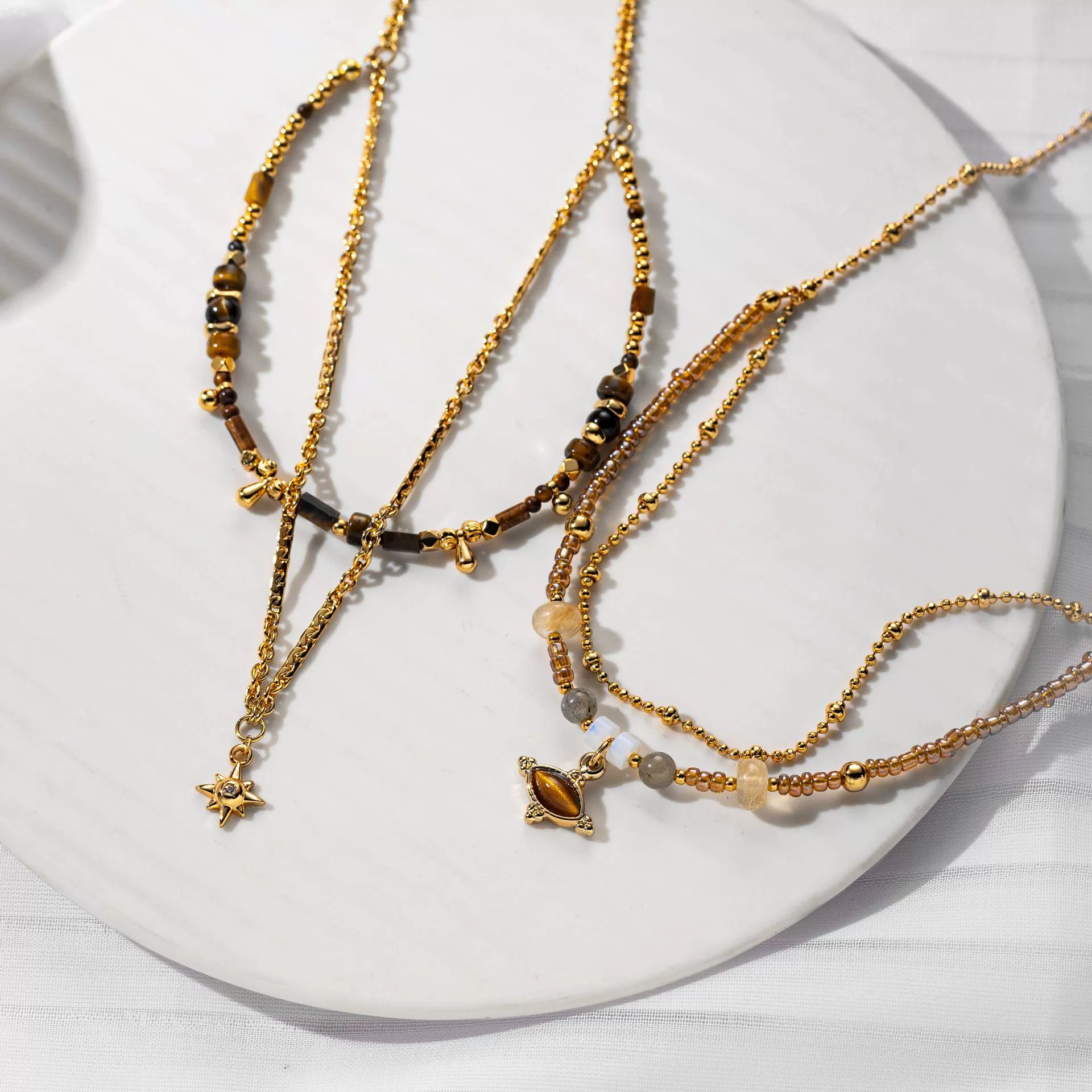 livke-tiger-eye-bead-gold-necklace LIVKE’s tiger eye bead necklace with gold and zirconia accents, styled with a linen dress for boho everyday elegance.