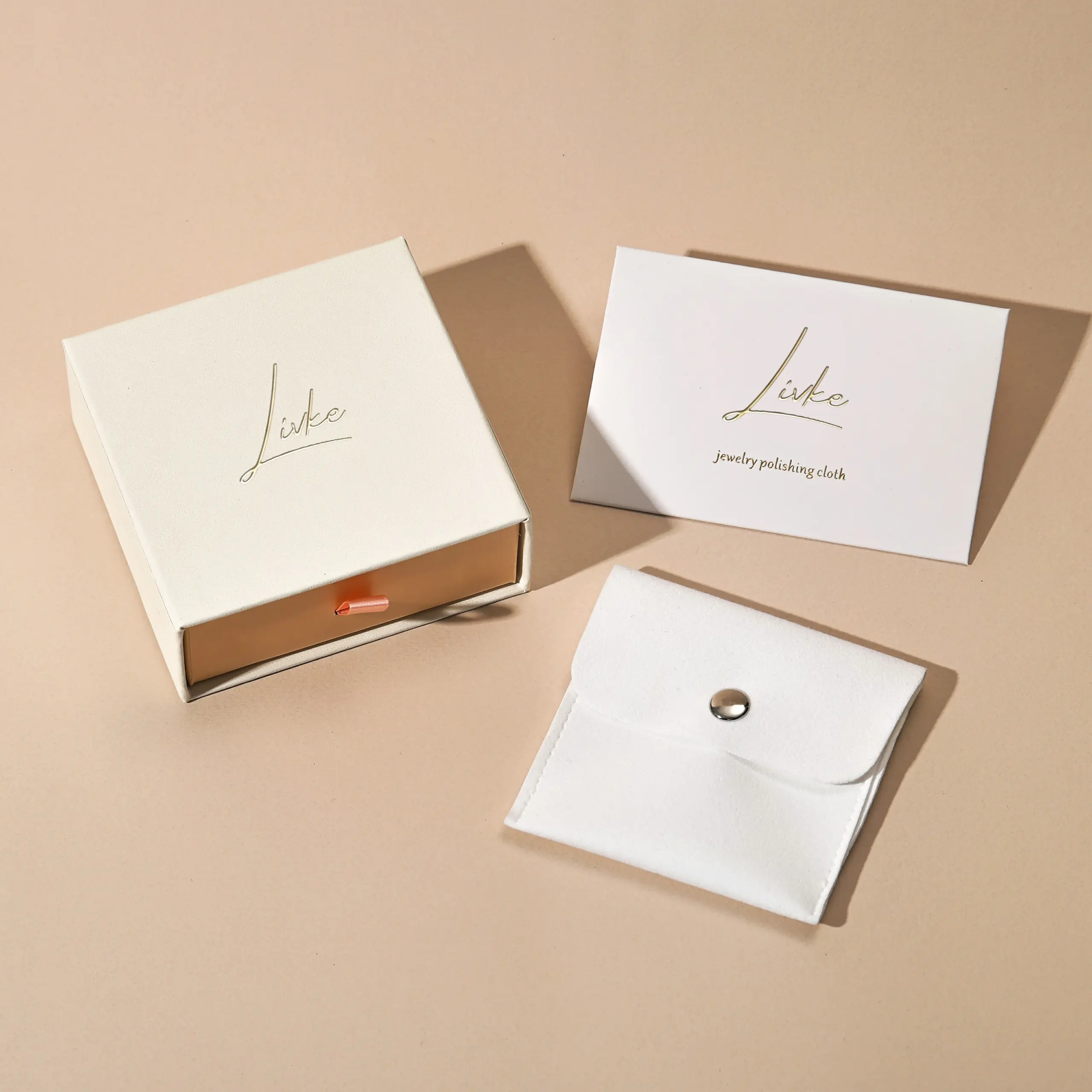 gold-foil-jewelry-care-set-flatlay Beige drawer box open with polishing cloth, necklace and ring on velvet background