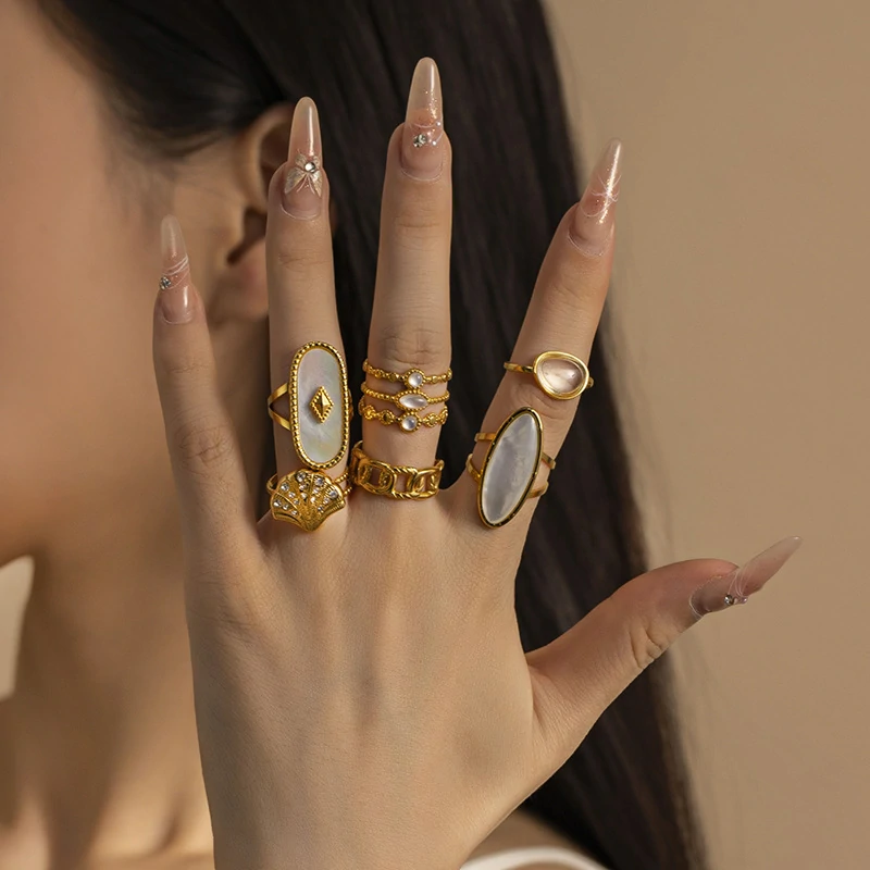 Tanned hand wearing LIVKE shell ring layered with thin gold bands against ocean waves