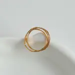 Three layered brass rings with spiral/chain/wave designs in 18K gold plating, stacked on a wooden tray for boho style