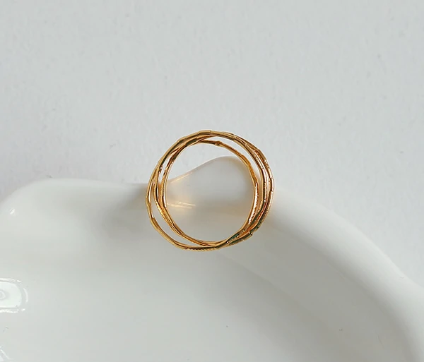 Three layered brass rings with spiral/chain/wave designs in 18K gold plating, stacked on a wooden tray for boho style