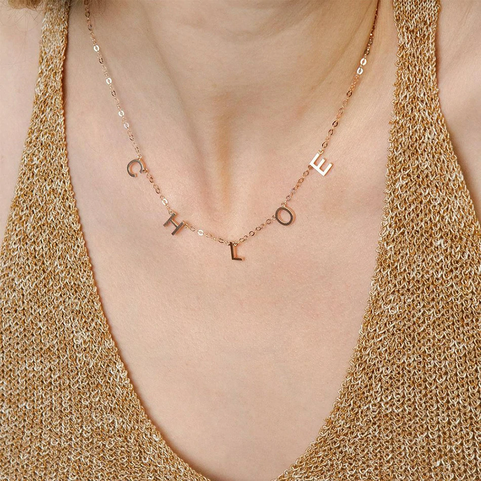 Gold alphabet necklace layered with 4 initials 'LIVK' on collarbone