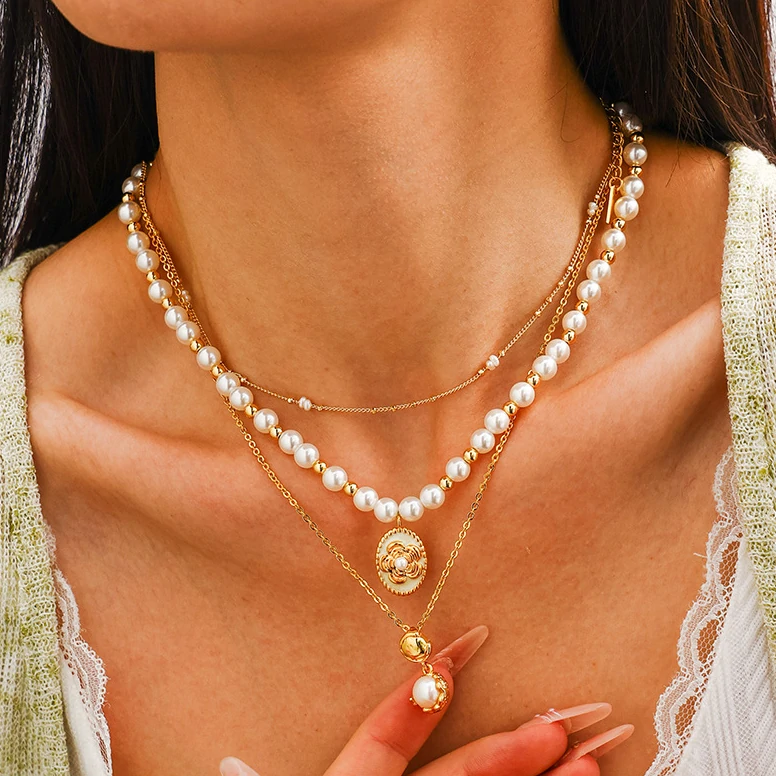 livke-gold-pearl-brass-necklace-vintage-layering (3) Woman wearing LIVKE gold plated pearl necklace with silk blouse and tailored blazer, showcasing vintage-inspired office to evening jewelry