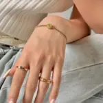 Adjustable layered bracelet with green braided cord, gold bead chains, and olive stone pendant on linen fabric, showing hypoallergenic clasp and boho styling for daily wear