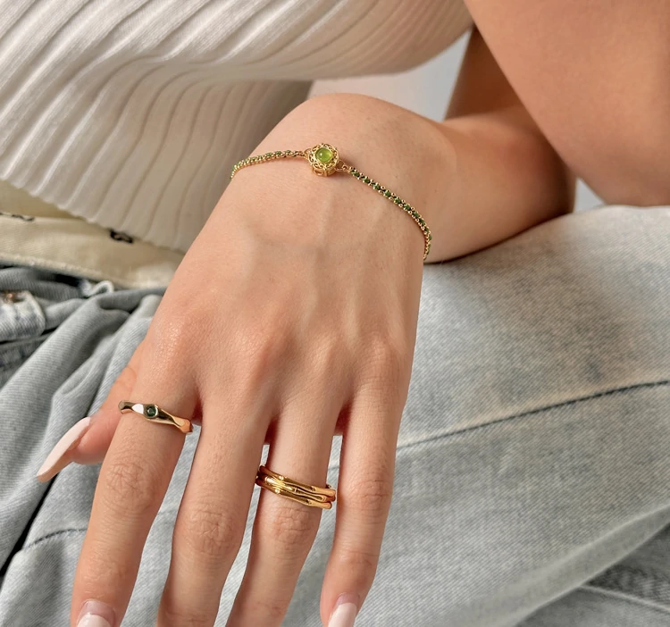 Adjustable layered bracelet with green braided cord, gold bead chains, and olive stone pendant on linen fabric, showing hypoallergenic clasp and boho styling for daily wear