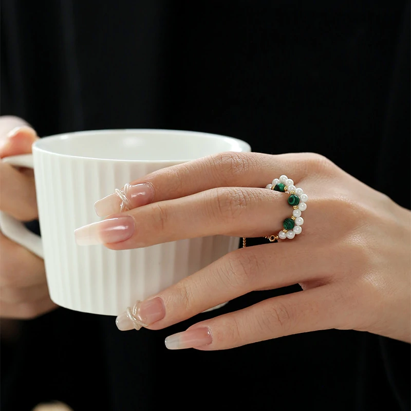 Hand wearing LIVKE adjustable wrap ring with pearls and green aventurine, layered with slim bands for boho chic style