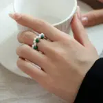 Hand wearing LIVKE adjustable wrap ring with pearls and green aventurine, layered with slim bands for boho chic style