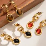 Layered 18K gold-plated tiger eye earrings with red/black/brown stone pendants on terrazzo backdrop, styled with leather cord necklaces