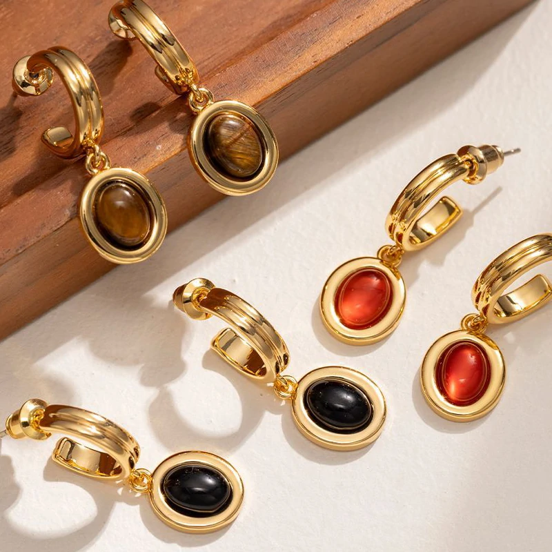 Layered 18K gold-plated tiger eye earrings with red/black/brown stone pendants on terrazzo backdrop, styled with leather cord necklaces