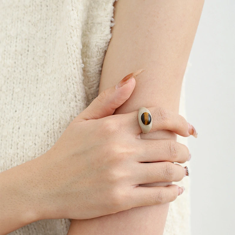 Hand wearing LIVKE adjustable tiger's eye ring layered with slim bands, showcasing bohemian power jewelry on desert-toned fabric