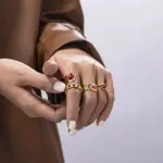 Hand wearing LIVKE red agate titanium ring with textured gold band in boardroom setting, showcasing power jewelry for professionals