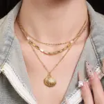 Natural tumbled shell pendant on 18K gold-plated chain styled with linen shirt and jeans at beachside café