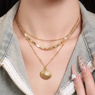 Natural tumbled shell pendant on 18K gold-plated chain styled with linen shirt and jeans at beachside café