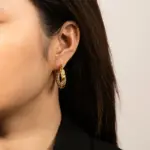 Gold twisted hoop earrings catching sunlight with layered necklaces on tanned skin