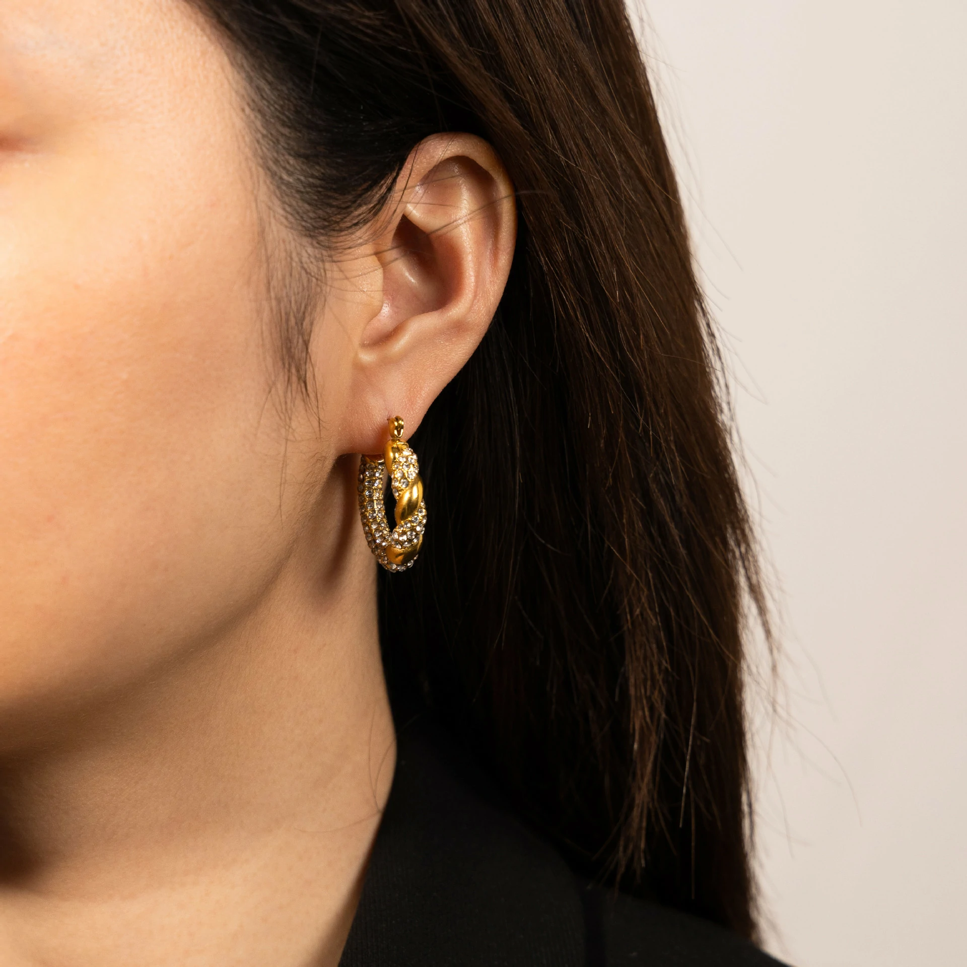 Gold twisted hoop earrings catching sunlight with layered necklaces on tanned skin