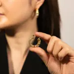 Gold twisted hoop earrings catching sunlight with layered necklaces on tanned skin