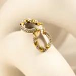 Gold twisted hoop earrings catching sunlight with layered necklaces on tanned skin