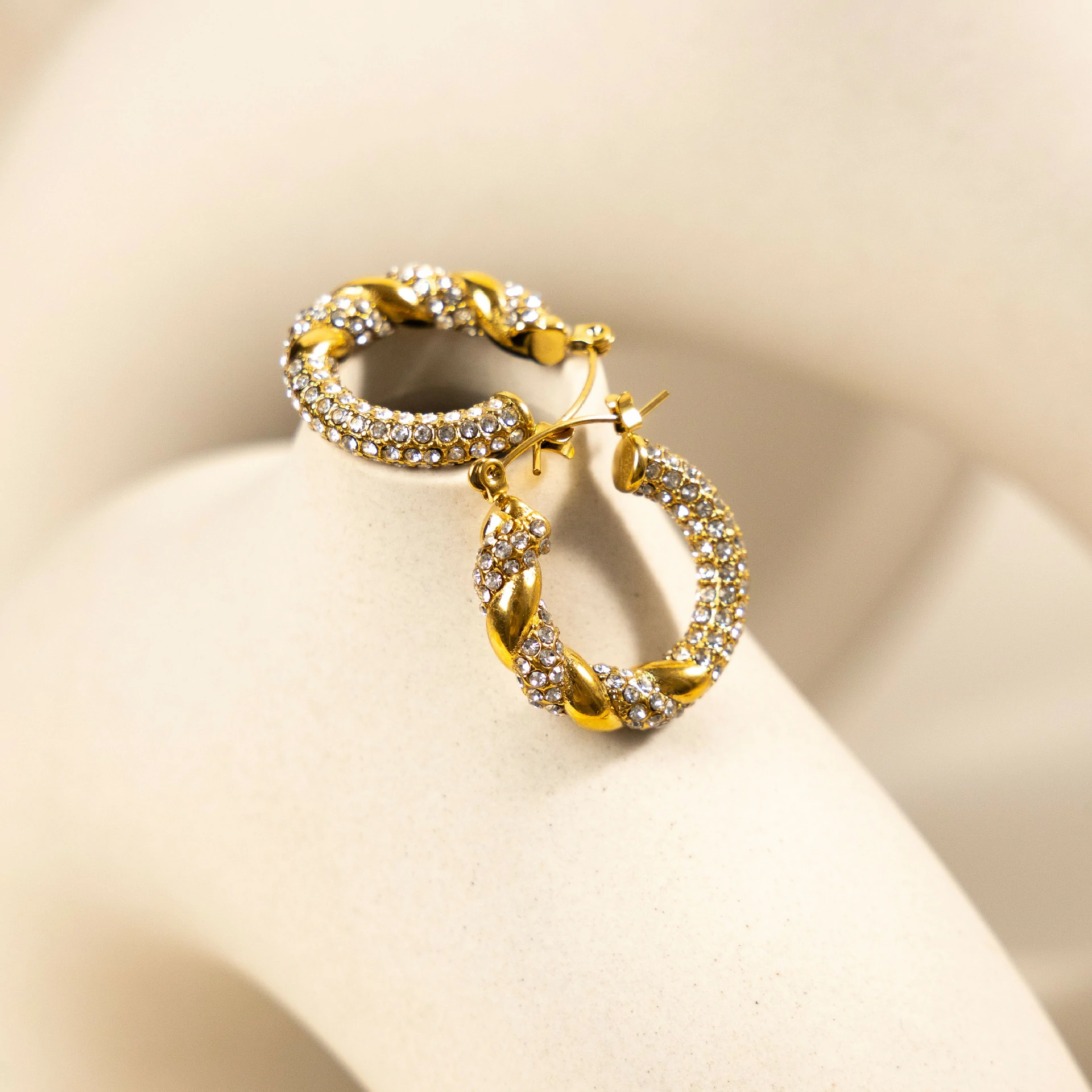 Gold twisted hoop earrings catching sunlight with layered necklaces on tanned skin