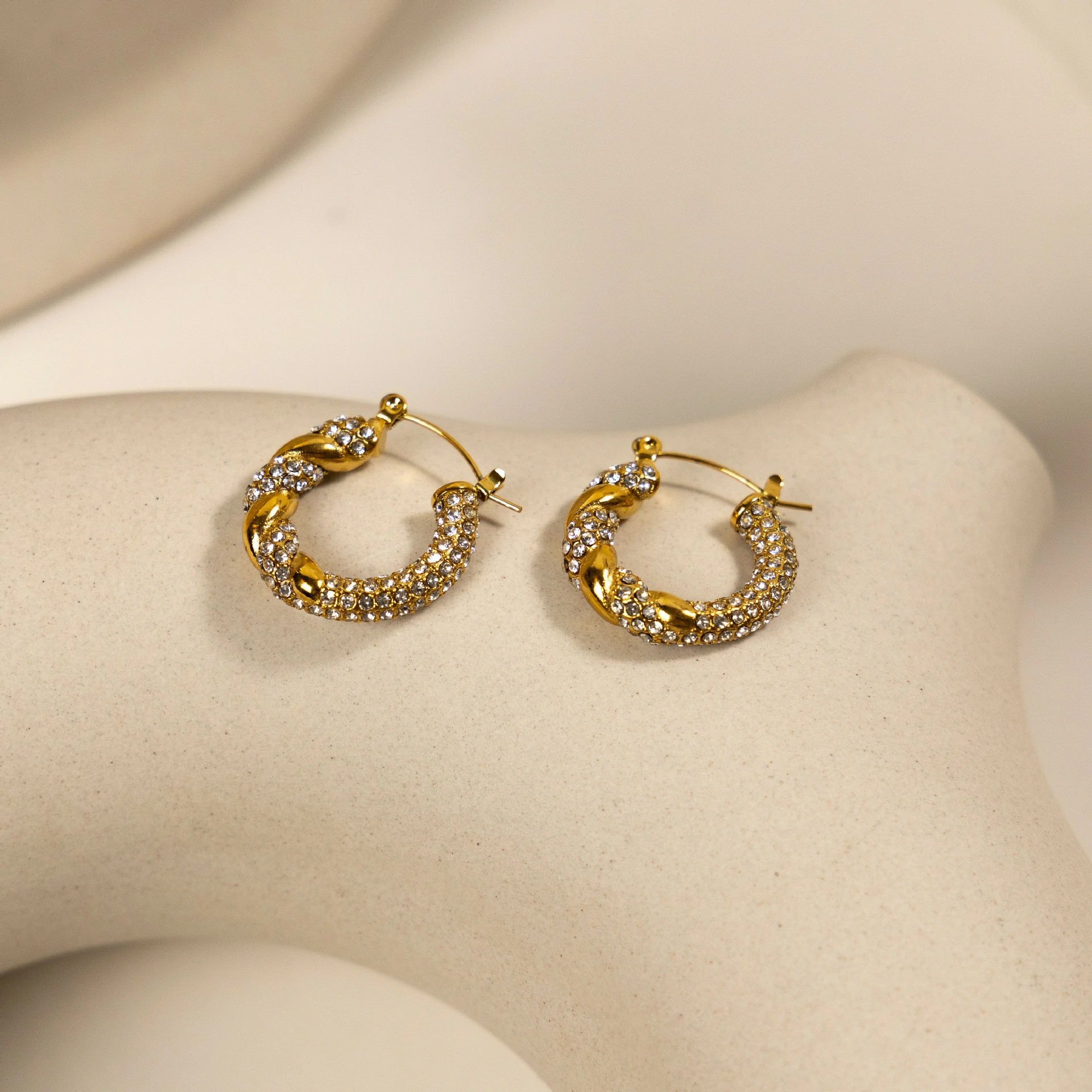 Gold twisted hoop earrings catching sunlight with layered necklaces on tanned skin