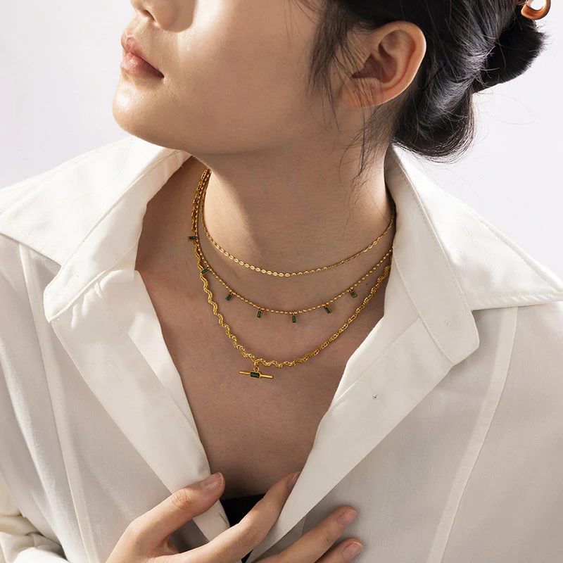 LIVKE chunky brass chain necklace with emerald-cut green zirconia pendant styled with black turtleneck for retro-modern elegance.