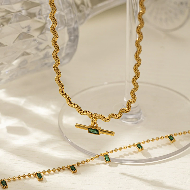 LIVKE chunky brass chain necklace with emerald-cut green zirconia pendant styled with black turtleneck for retro-modern elegance.