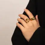 Woman wearing LIVKE gold love signet ring while holding cappuccino in Parisian café, showcasing stackable jewelry styling