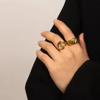 Woman wearing LIVKE gold love signet ring while holding cappuccino in Parisian café, showcasing stackable jewelry styling