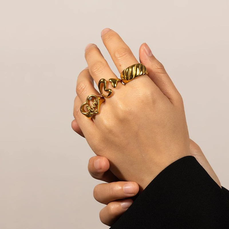 Woman wearing LIVKE gold love signet ring while holding cappuccino in Parisian café, showcasing stackable jewelry styling