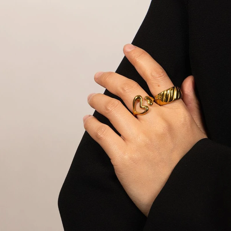 Woman wearing LIVKE gold love signet ring while holding cappuccino in Parisian café, showcasing stackable jewelry styling